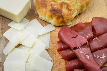 Charcuterie board with italian bresaola cured beef, grana padano cheese flakes and focaccia bread close up.