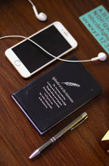 notebook, cell phone, headphones and a pen on a wooden table