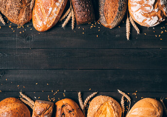 Bread border on wood background with copy space. Vertical composition of whole grain loaves with ears. Different kinds of bread. Bakery, cooking and grocery store concept.
