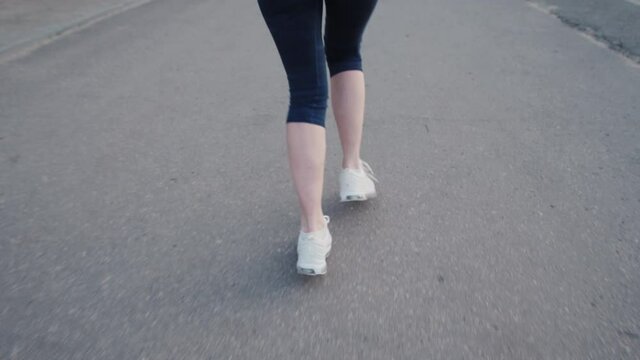 Close up woman legs running on concrete footpath at public park with sunlight in the background.