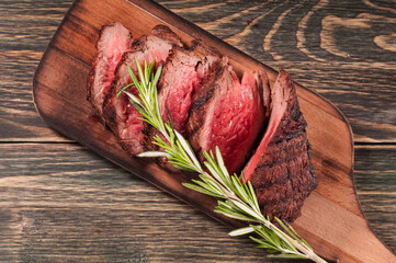 Medium ribeye slices steak on the wooden tray with  rosemary, wooden background