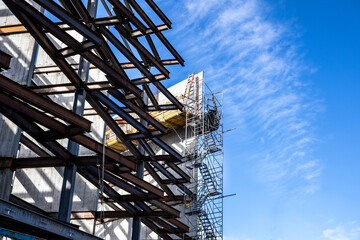 Partial construction of an industrial multilevel building. Steel framing /metal beams visible with walkways and ladders. Corner view of half built structure with blue sky. No people.