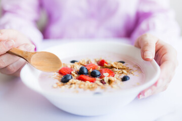 Woman eating fresh muesli with milk and fruits at the table.