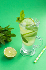 Infused water or cold lemonade with lime, ice and  mint  in the glass  on the green background. Location vertical. Copy space.