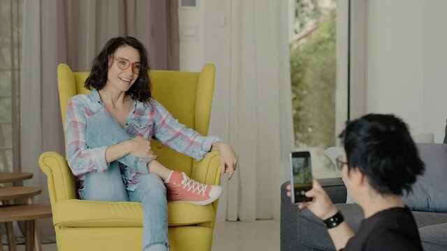 young female doing different poses for photographer taking pictures on smartphone. Rbbro amateur photo session for model at home on armchair couch. concept camera, quarantine, memories.