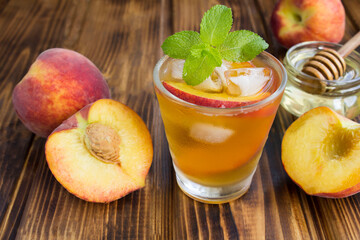 Cold tea with peaches in the glass on the brown wooden background. Closeup.
