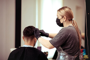 Close up hairdresser with security measures for Covid-19, cuts a man  social distance, cutting hair with a medical mask.