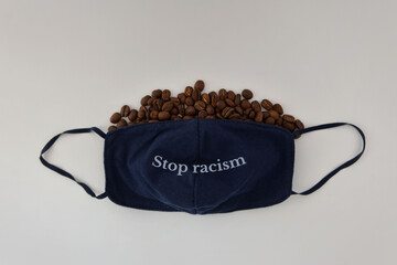 Dark protective mask with phrase stop racism and coffee beans on a gray background