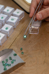 Hand holding a emerald gemstone with jewelry forceps. Gemologist workspace.
