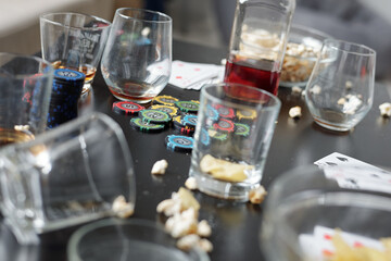 Close-up of empty dirty glasses, poker chips, playing cards and popcorn on table after poker party