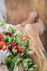 Obraz na płótnie Canvas Selective focus of beautiful flowers bouquet on woman slim legs. Morning light, greeting card with copy space.