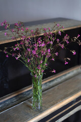 Bunch of wild flowers in a transparent vase up of an old piano