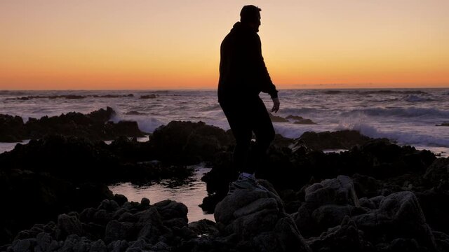 Young men warrior monk practicing silhouette tai chi karate kung Fu on the rocky stones horizon at sunset or sunrise. Art of self-defense. Silhouette on a background of dramatic epic waves