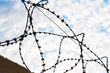 Barbed wire, against a background of white clouds and blue sky. The concept of non-freedom. Prison, incarceration.