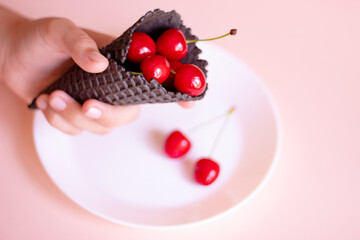 a hand holding an ice cream cone with cherries inside