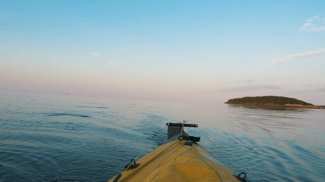 tail of yellow kayak in motion, boat floats on quiet lake at sunset on background of island, outdoor activities