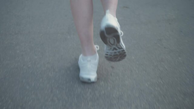 Close up woman legs running on concrete footpath at public park with sunlight in the background.
