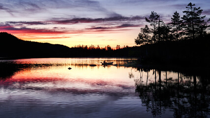 Fisherman in a row boat in a beautiful sunset. Red, orange and blue colors against black silhouette makes the mystic in the photo. Shot in Norway, Nordmarka, Oslomarka. Crips and clear colors.