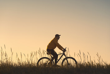 Obraz premium Silhouette of a cyclist. He rides through the meadow.