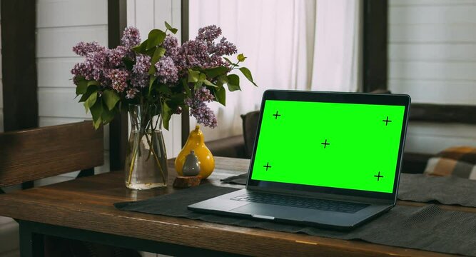 On a wooden table in the living room in the house is a laptop. A convenient and cozy place to work. Computer screen with dot tracking. Home furnishings. The interior of a residential building.