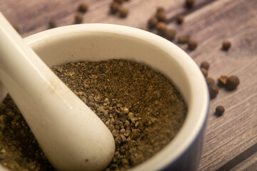 Allspice in a ceramic mortar and scattered allspice on a wooden table. Close up.
