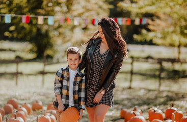 Young pretty mother with long hair posing with cute little blond son with pumpkin at the pumpkin's field. Copy space.