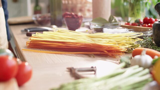 Close up tilt down shot of hands of male cook throwing bunch of uncooked homemade spaghetti on kitchen table