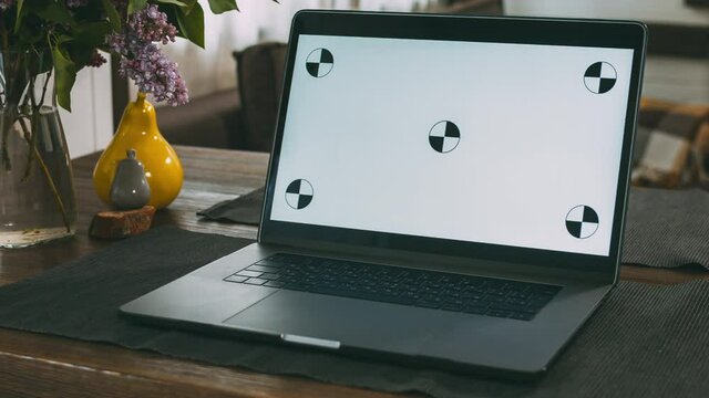 On a wooden table in the living room in the house is a laptop. A convenient and cozy place to work. Computer screen with dot tracking. Home furnishings. The interior of a residential building.