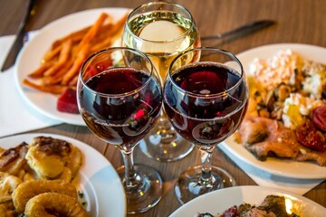 Three glasses of red and white wine on the table with delicatessen on plates in restaurant.