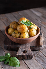 Young roasted potatoes with basil in a ceramic bowl on a wooden table