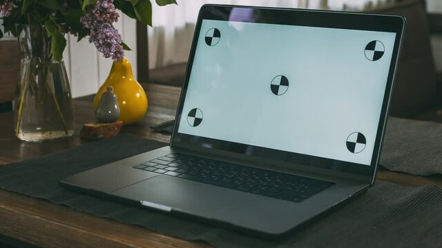 On a wooden table in the living room in the house is a laptop. A convenient and cozy place to work. Computer screen with dot tracking. Home furnishings. The interior of a residential building.