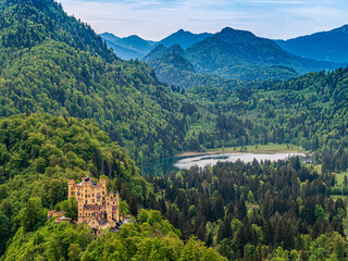 Schloss Hohenschwangau mit Alpsee und bewaldeten Bergen bei leicht bewölktem Himmel