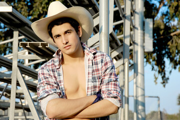 A sexy young cowboy poses with his shirt open to show his masculine and muscular body.  