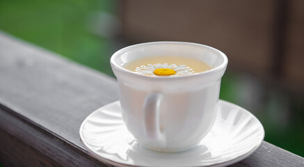 Green tea in a white mug with a chamomile inside on a brown wooden background