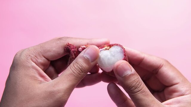 Man hand taking kin off from a Lychee on a pink background top down.