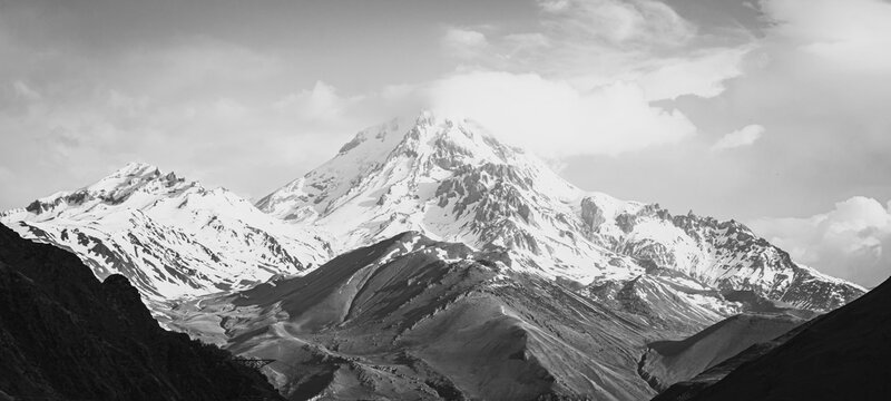 Background image of Kazbek peak ith snowy top surounded by the mountains in spring time. Dramatic landscapes of Kazbegi national park. Hiking and climbing in caucasus.2020
