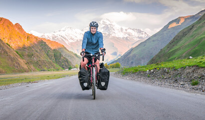 Male cyclist is on touring bicycle front side cycling bicycle touring with mountains white peaks background in summer or spring. Cycling holidays around caucasus in Georgia