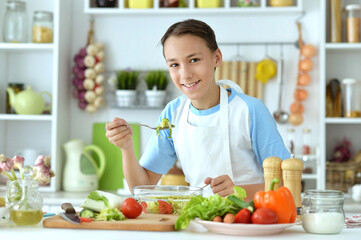 Cute boy preparing salad on kitchen table at home