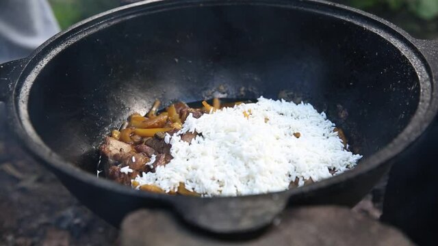 cooking Uzbek pilaf in a cauldron on fire in nature during a hike, national food, hiking food, nobody