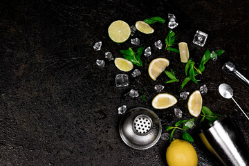 popular alcohol drink summer cocktail mojito creative composition with lemon slices, ice cubes, mint leaves and bar tool on dark background