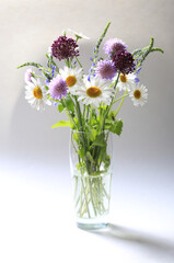 Bouquet of beautiful multicolored wildflowers in a glass vase on a light background