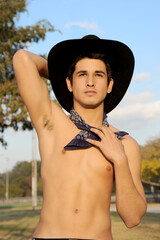 A handsome hispanic cowboy is wearing a black cowboy hat and posing as the sun shines on his...