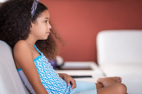 Multiracial small girl with beautiful curly hair watching TV at home