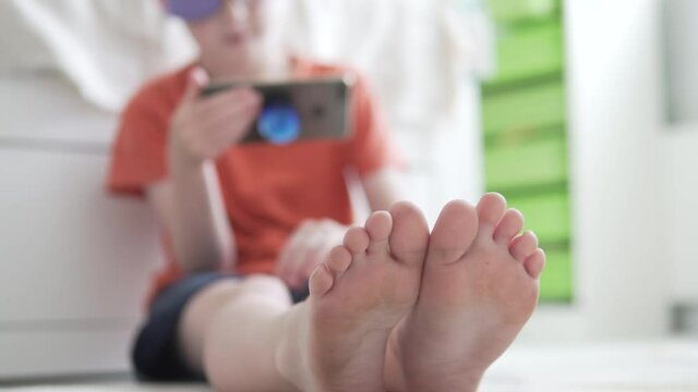 Boy watches video on mobile phone, focus on legs, baby blurred