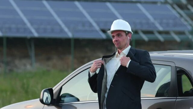 Cheerful worker in a helmet is dancing near the car. Sharply answers a phone call in the earpiece. Playful mood at the end of the day.