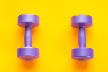 Two purple dumbbells lie separately on a yellow background