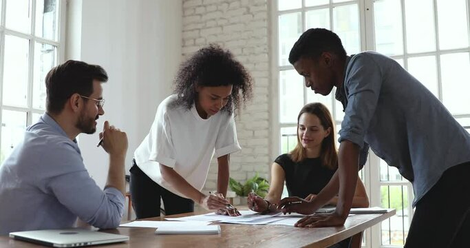 Young creative african and caucasian colleagues group analyze paperwork talk work together at diverse team meeting, focused friendly business team brainstorm on project strategy at briefing table