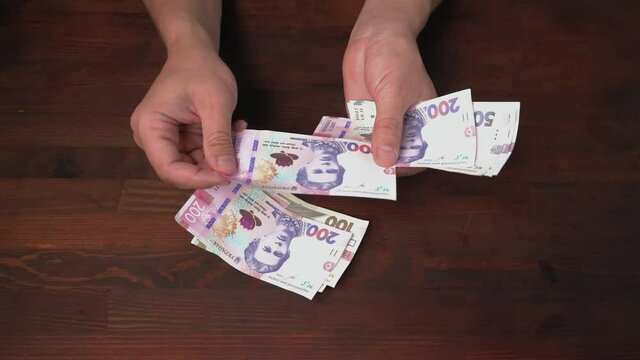 Man hands counting checking of new Ukrainian banknotes. New paper hryvnias different face value are on a brown wooden table. Cash money concept. prores 422. 