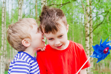 Two children share secrets. The boy whispers a secret in his brother's ear.