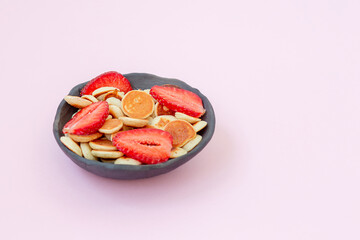Bowl with pancake cereal with strawberry on ink background.